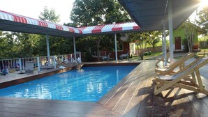 A swimming pool with a covered area, lounge chairs, and a small building in the background. - Rai Phurak Resort (Suan Phueng)