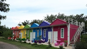 A row of colorful houses with white doors and windows, each with a small porch and potted plants. - Rai Phurak Resort (Suan Phueng)
