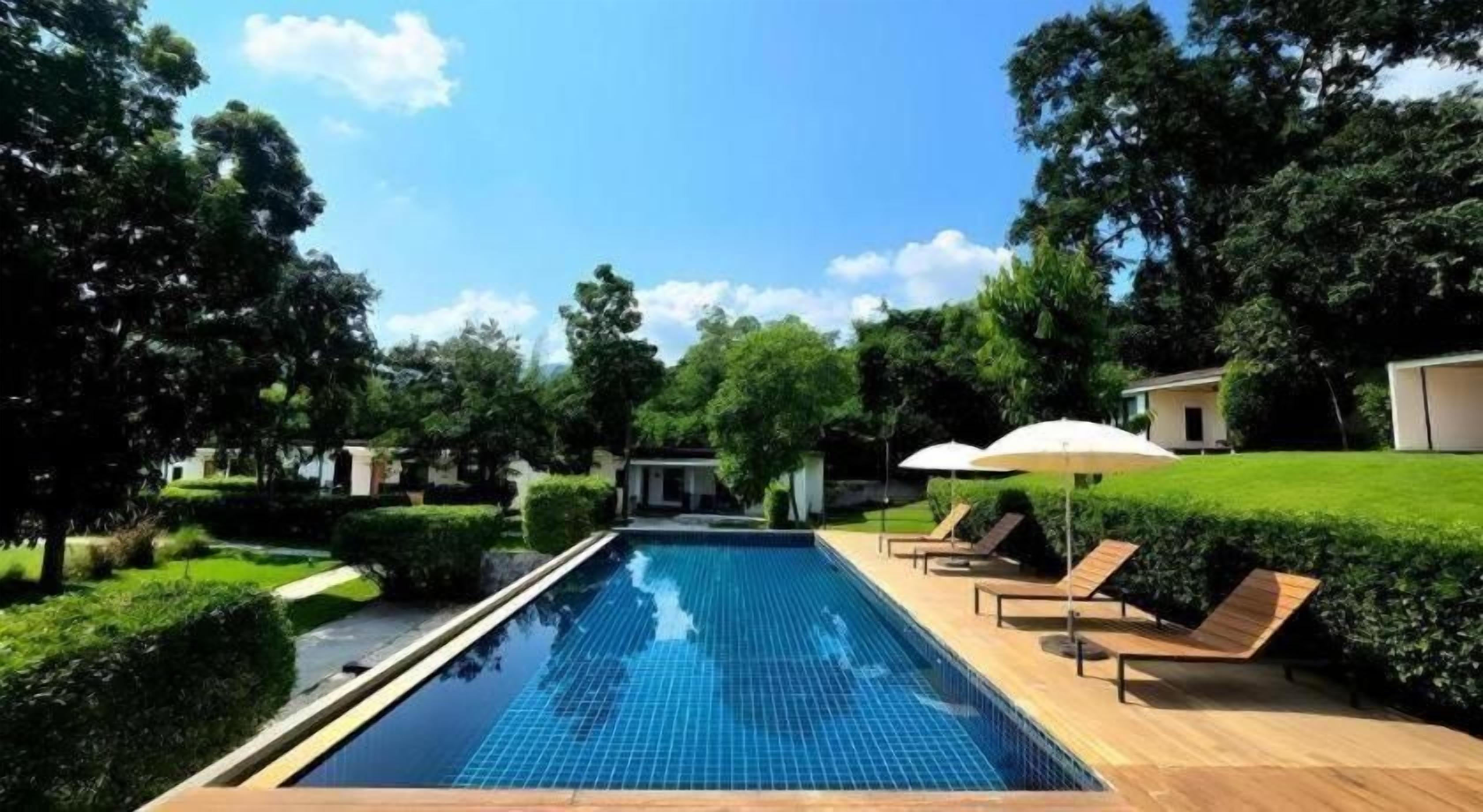 A rectangular swimming pool with a tiled edge, surrounded by a wooden deck and lounge chairs with umbrellas.