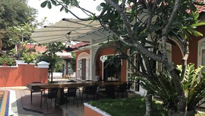 Un espace extérieur aménagé pour les repas, avec une piscine, entouré de verdure et doté d’une terrasse couverte.