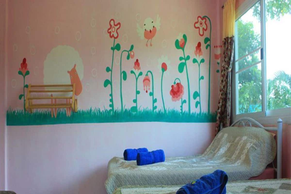 Quarto com duas camas, parede rosa com mural de tema natural e janela com cortinas.