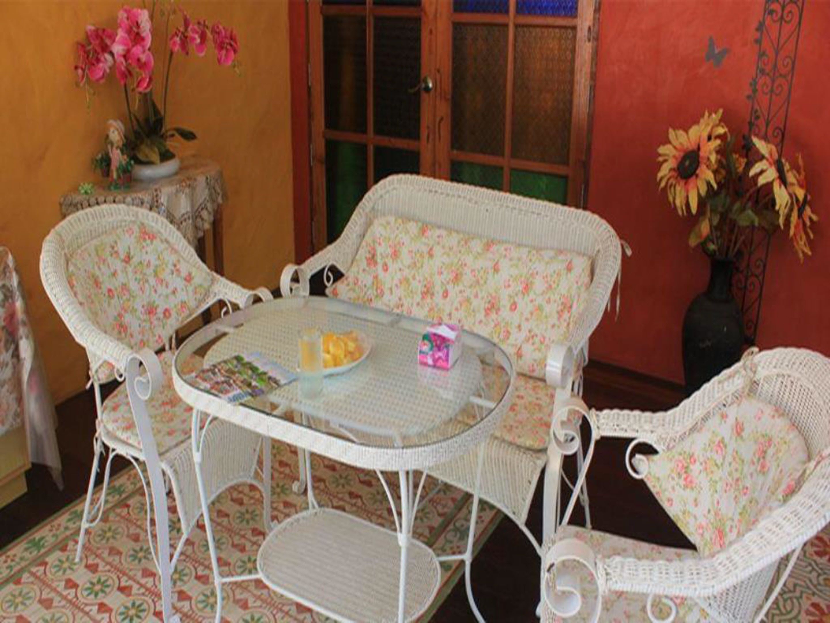 Juego de comedor de mimbre con cojines estampados y una mesa de vidrio, rodeado de baldosas con diseño.