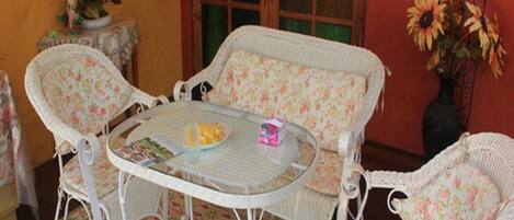 A wicker dining set with floral cushions and a glass table, surrounded by patterned floor tiles.