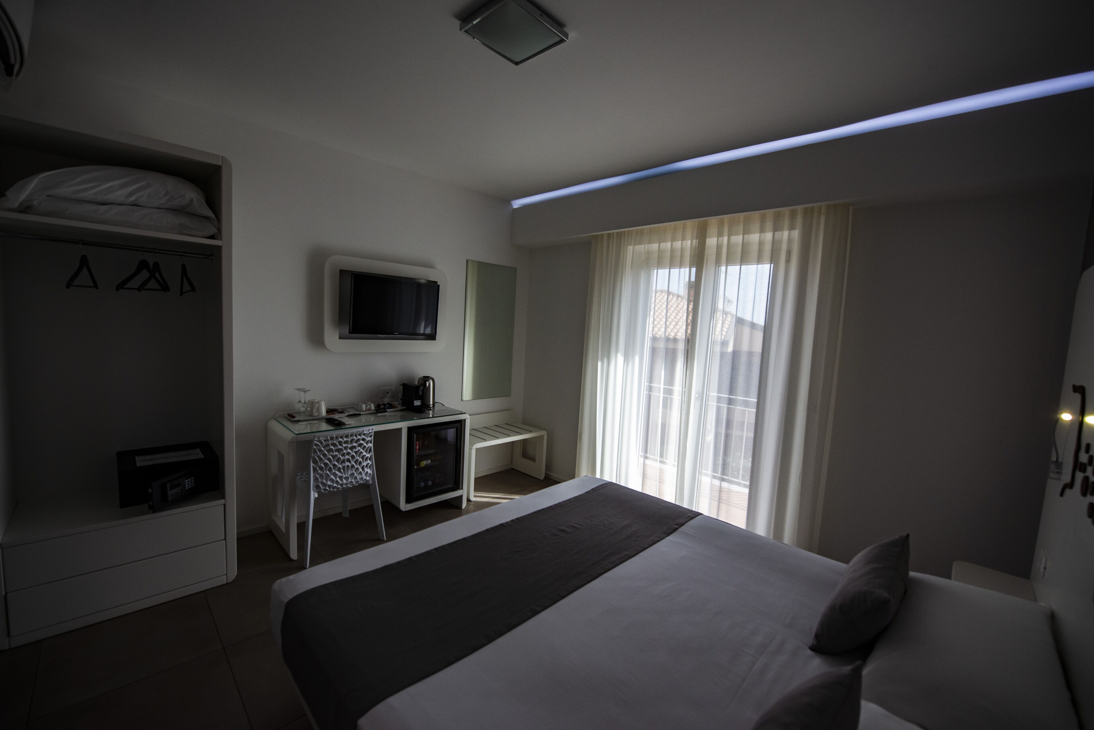 A hotel room with a bed, a desk with a computer, a TV, and a wardrobe.