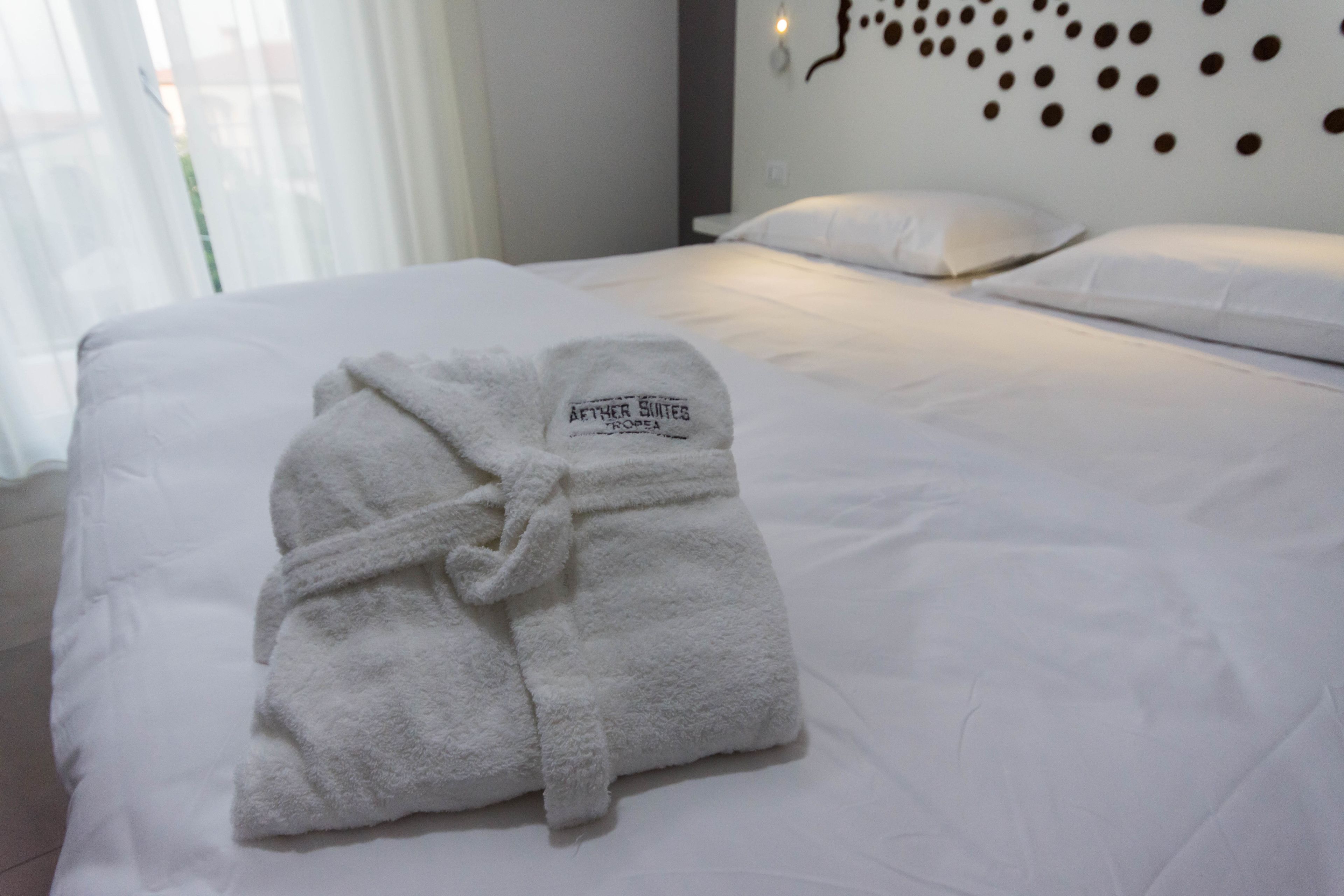 A neatly made bed with a white bathrobe on it, a white pillow, and a wall with a circular pattern.