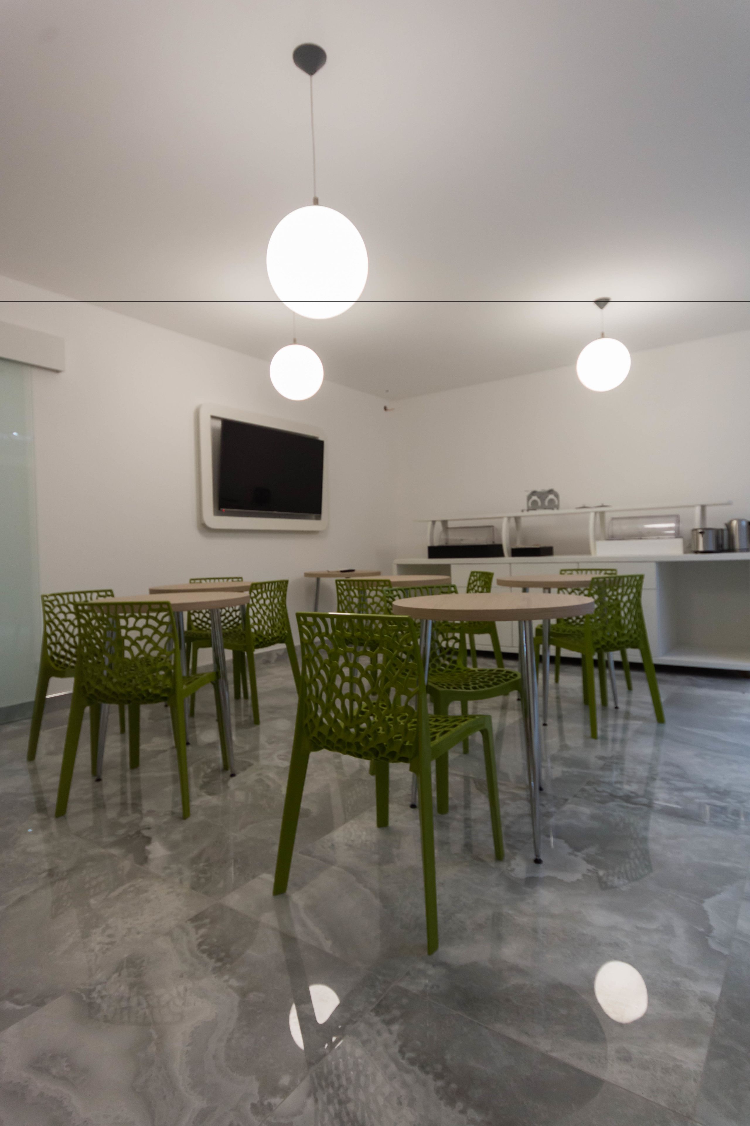 Un espace de salle à manger moderne avec des chaises vertes, une table blanche et des luminaires suspendus.