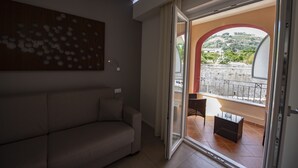 A modern living room with a sofa, a ceiling light, and a view through a glass door to an outdoor balcony with a table and chairs. - Aether Suites Tropea (Tropea)