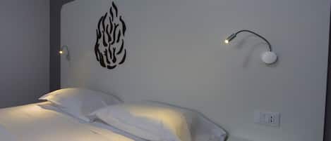 A neatly made bed with white linens, a wall-mounted light fixture, and a power outlet.