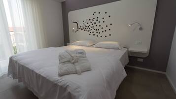 Una habitación de hotel moderna con una cama grande, ropa de cama blanca, un cabecero con un original estampado de puntos, una bata sobre la cama y una mesita de noche pequeña.