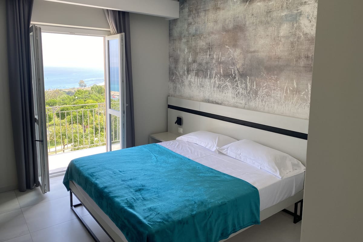 Une chambre à coucher avec un lit, une vue sur l’extérieur et un grand tableau abstrait accroché au mur.