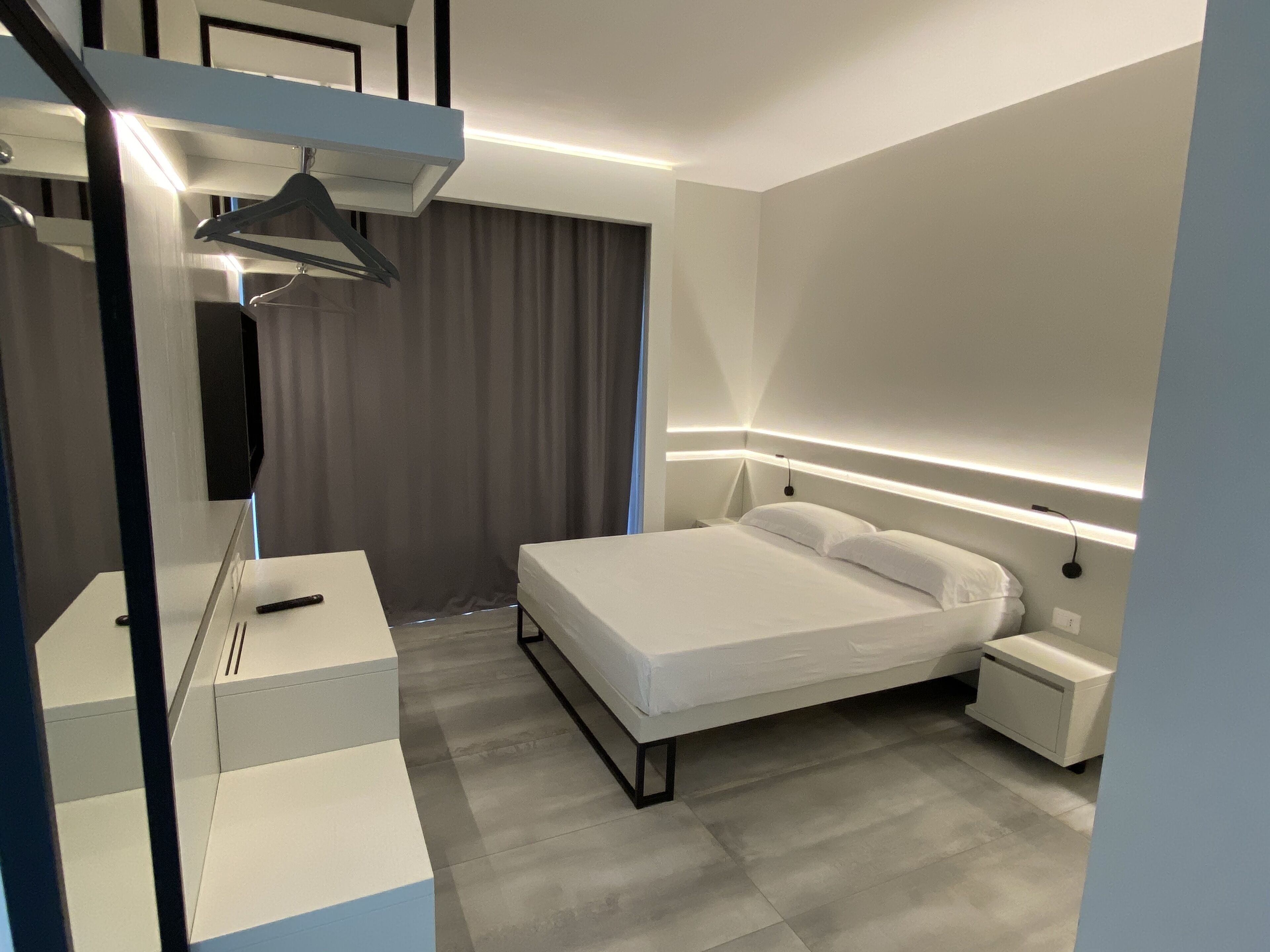 A modern bedroom with a bed, bedside tables, a desk, and a hanging light fixture.