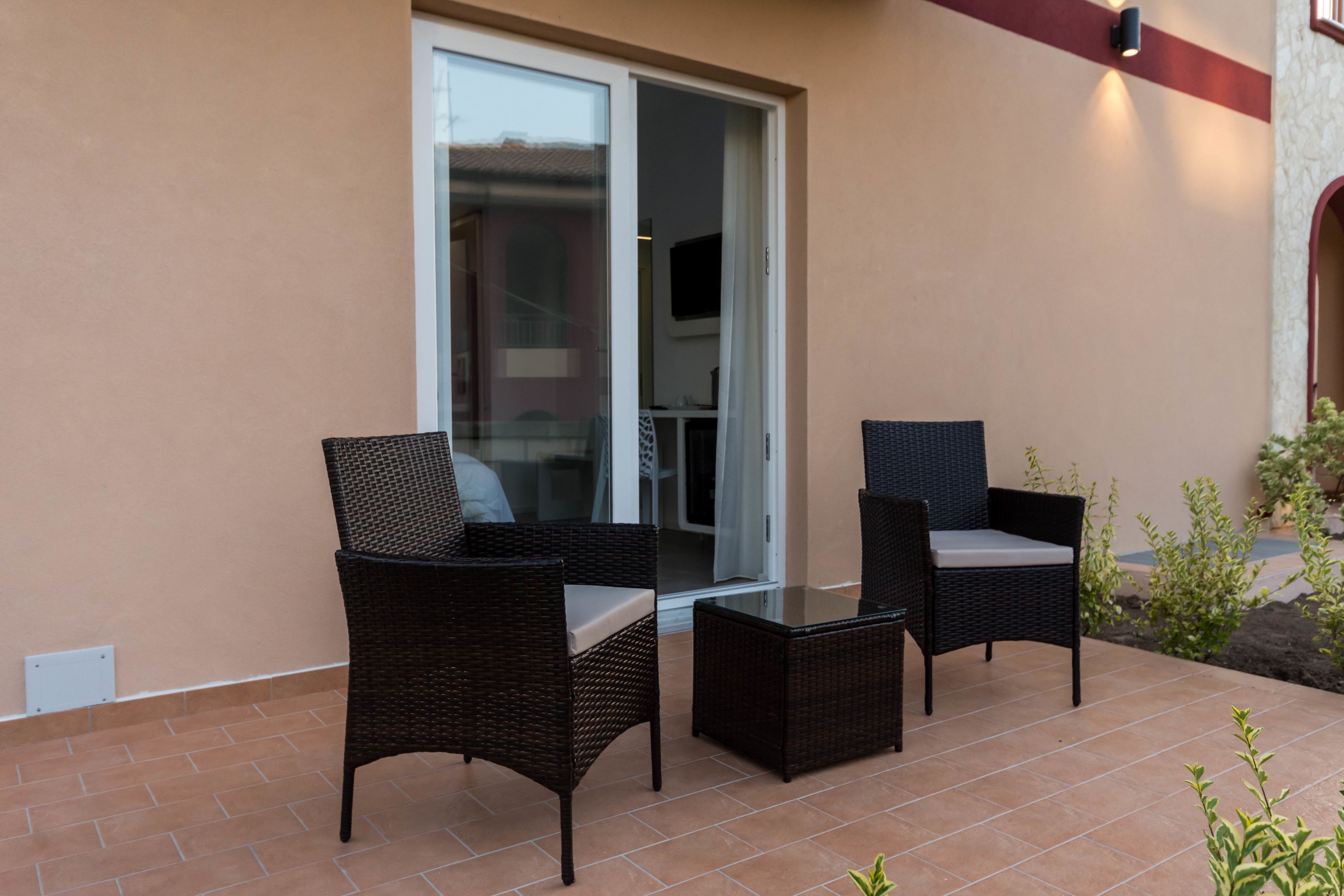 An outdoor patio with two wicker chairs and a small table, a sliding glass door, and a wall-mounted light fixture.