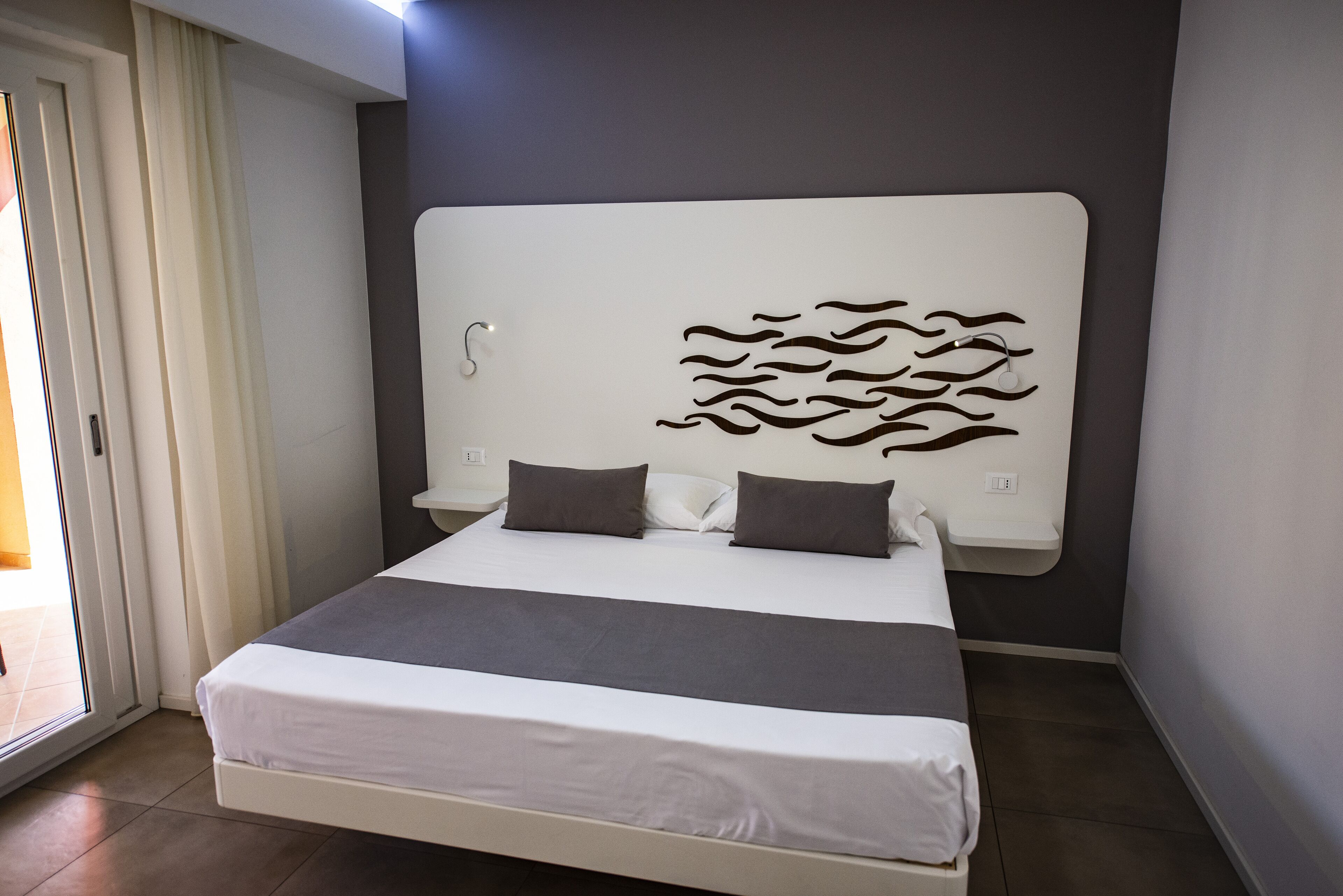 Un dormitorio moderno con una cama grande, dos almohadas, un cabecero con diseño de olas y una puerta corredera a la izquierda.