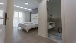 A modern hotel room with a large bed, a walk-in bathroom, and a view of the city. - Aether Suites Tropea (Tropea)