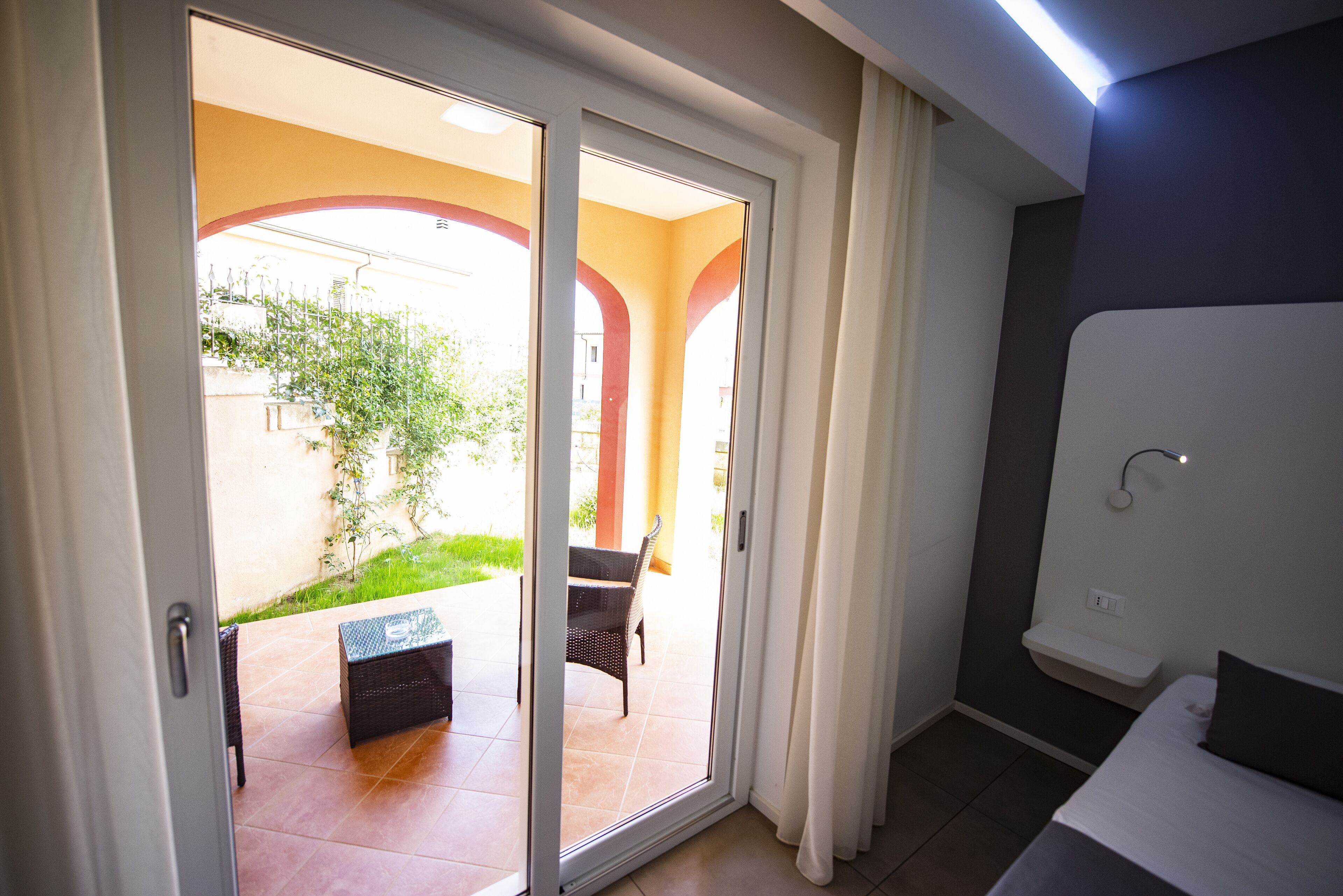Habitación de hotel con puerta corrediza de vidrio que da a un patio exterior con mesa y sillas.