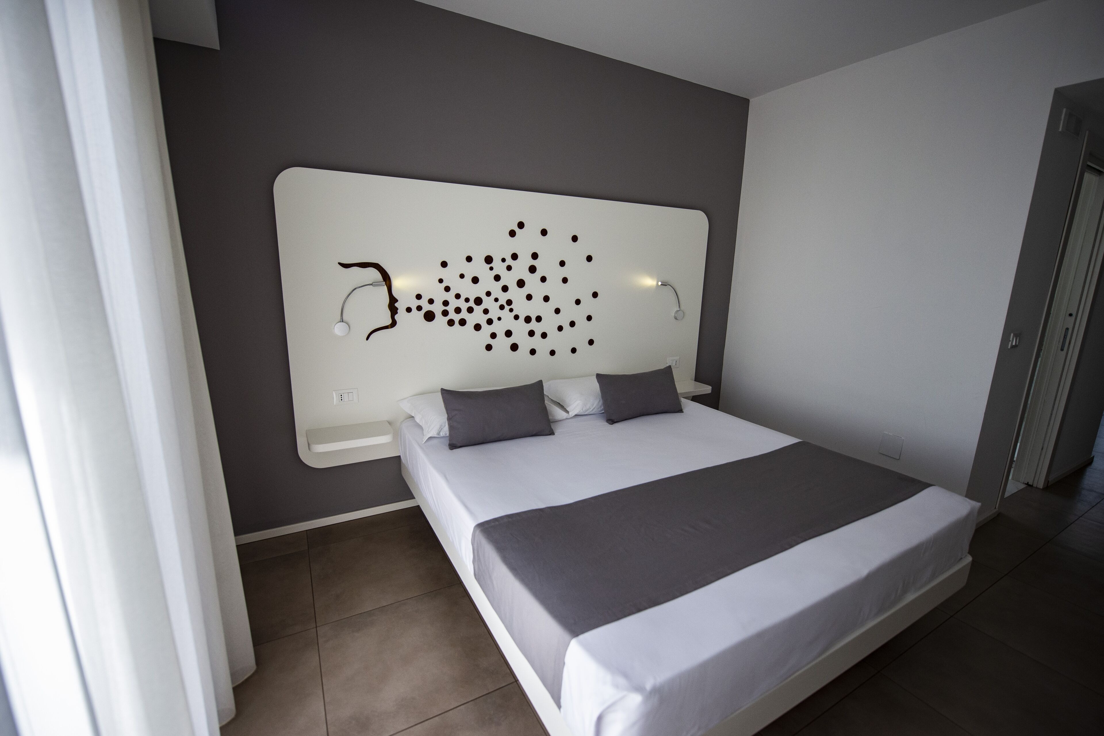 A modern bedroom with a large bed, a headboard with a unique design, and a nightstand with a lamp.