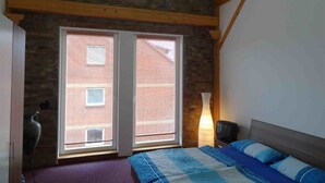 A bedroom with a bed, a nightstand, a lamp, and a window with blinds. - Ferienwohnung Nitschke Zum Nusshof (Ahrensfelde)