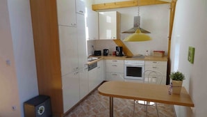 A compact kitchen with white cabinets, a wooden table, and a hanging yellow light fixture. - Ferienwohnung Nitschke Zum Nusshof (Ahrensfelde)