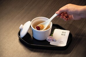 Une main tenant une cuillère au-dessus d’un bol de soupe, le bol étant recouvert d’un couvercle, et une carte se trouvant à côté.