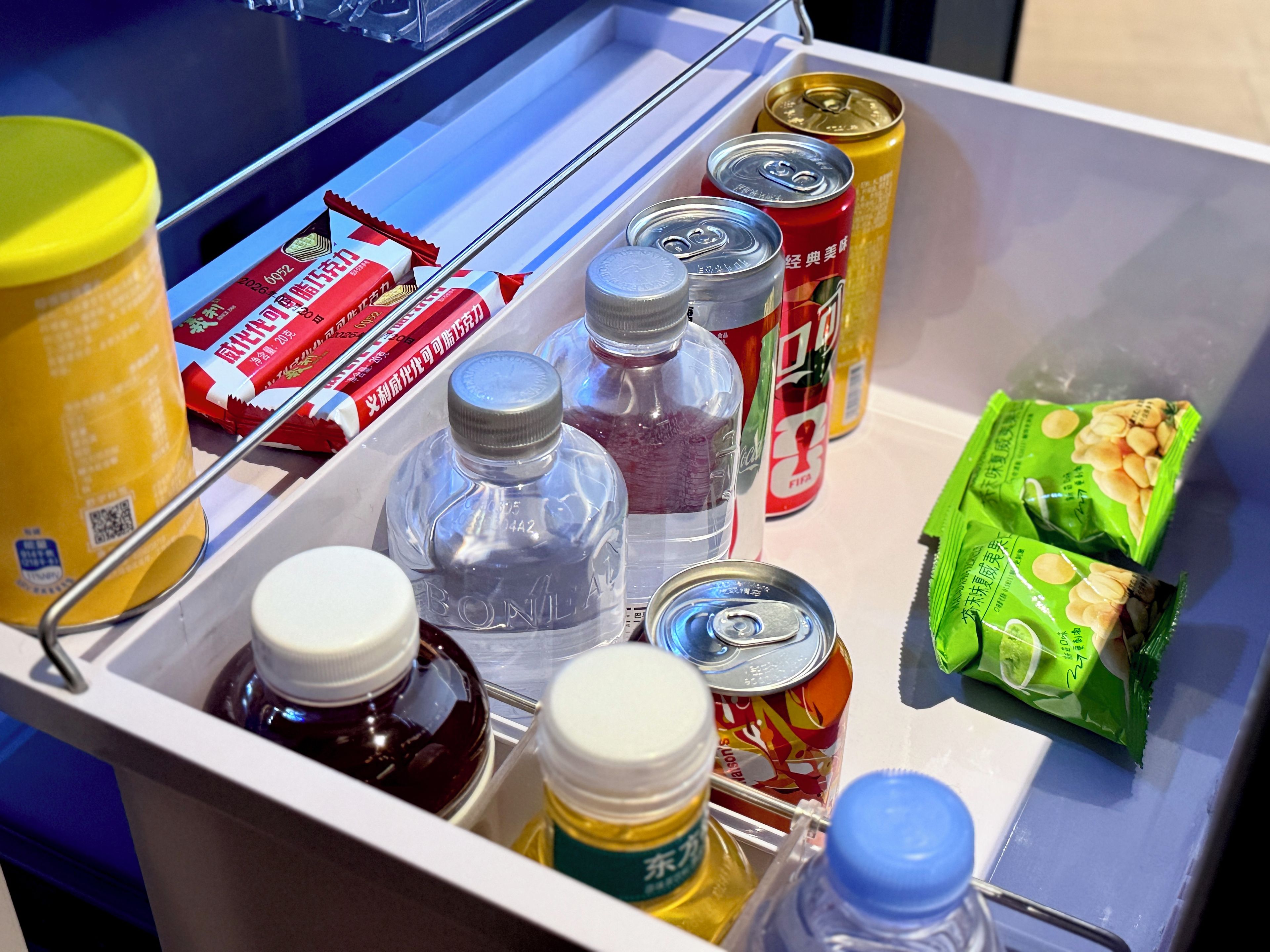 Un frigorifero contenente diversi alimenti e bevande, tra cui lattine, bottiglie e prodotti confezionati.