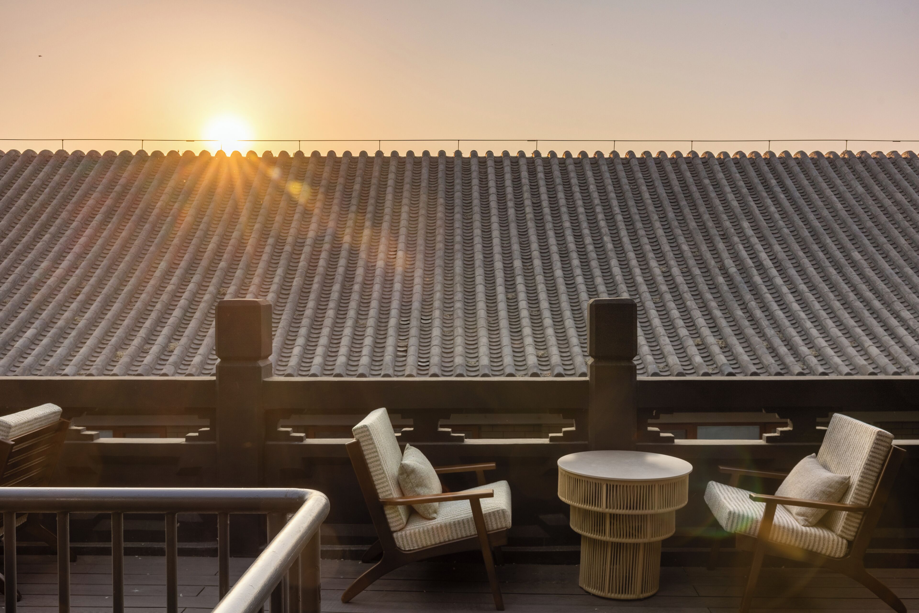 Une terrasse avec des chaises et une table, donnant sur un toit recouvert de tuiles.