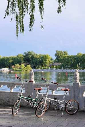 Deux vélos sont garés au bord d’un plan d’eau, avec une balustrade en pierre et un bâtiment traditionnel en arrière-plan.
