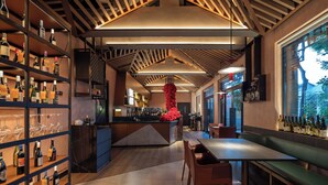 A modern bar with shelves of bottles and glasses, a central island with a red decorative piece, and a seating area with a view through large windows. - Blossom House Prince Kung's Mansion · Beijing Houhai (Beijing)