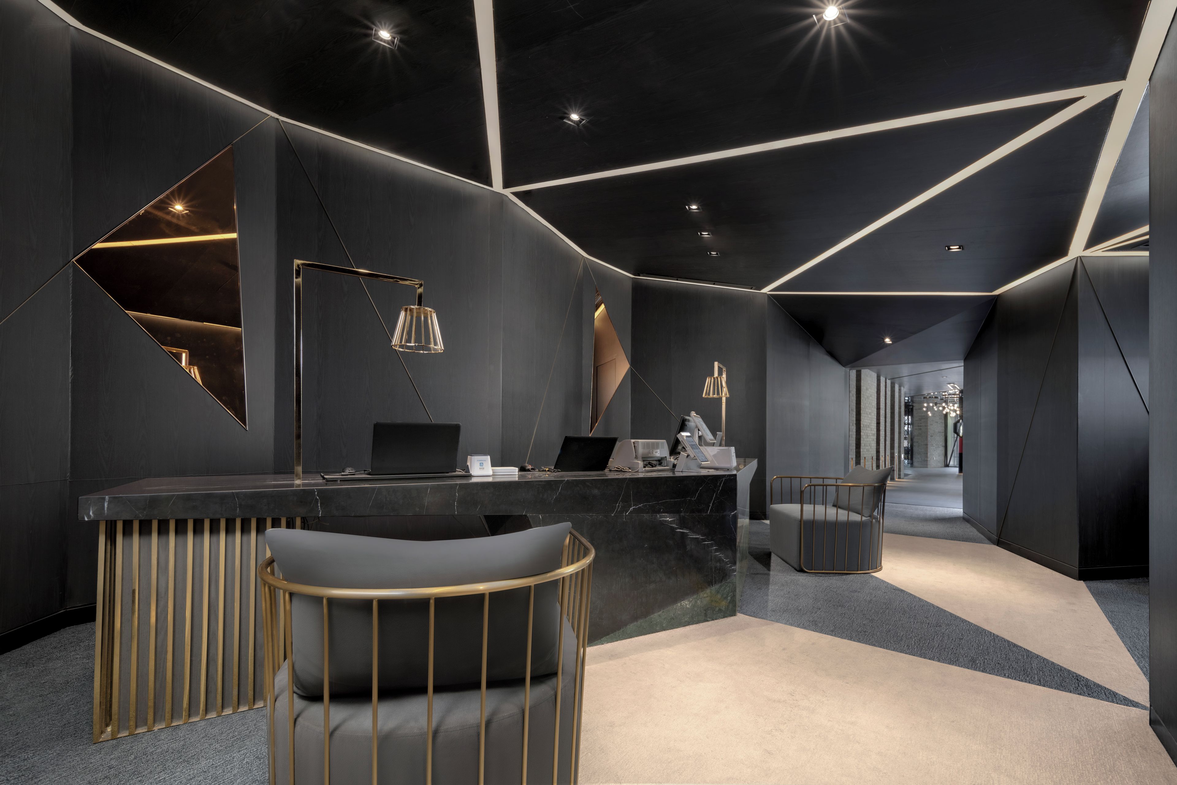 A modern reception area with a marble counter, two laptops, a desk lamp, and a seating area with a chair and a sofa.