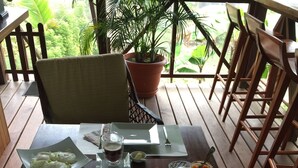 A dining table set with plates, cutlery, and various food items like fruits and bread, on an outdoor wooden deck with chairs and a potted plant. - Maya Hill Lodge (Mount Hope)