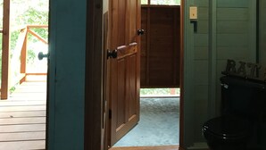 A wooden door leading to a room with a ceiling fan and a black toilet. - Maya Hill Lodge (Mount Hope)