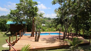 A wooden deck with a pool, surrounded by trees and a view of hills. - Maya Hill Lodge (Mount Hope)