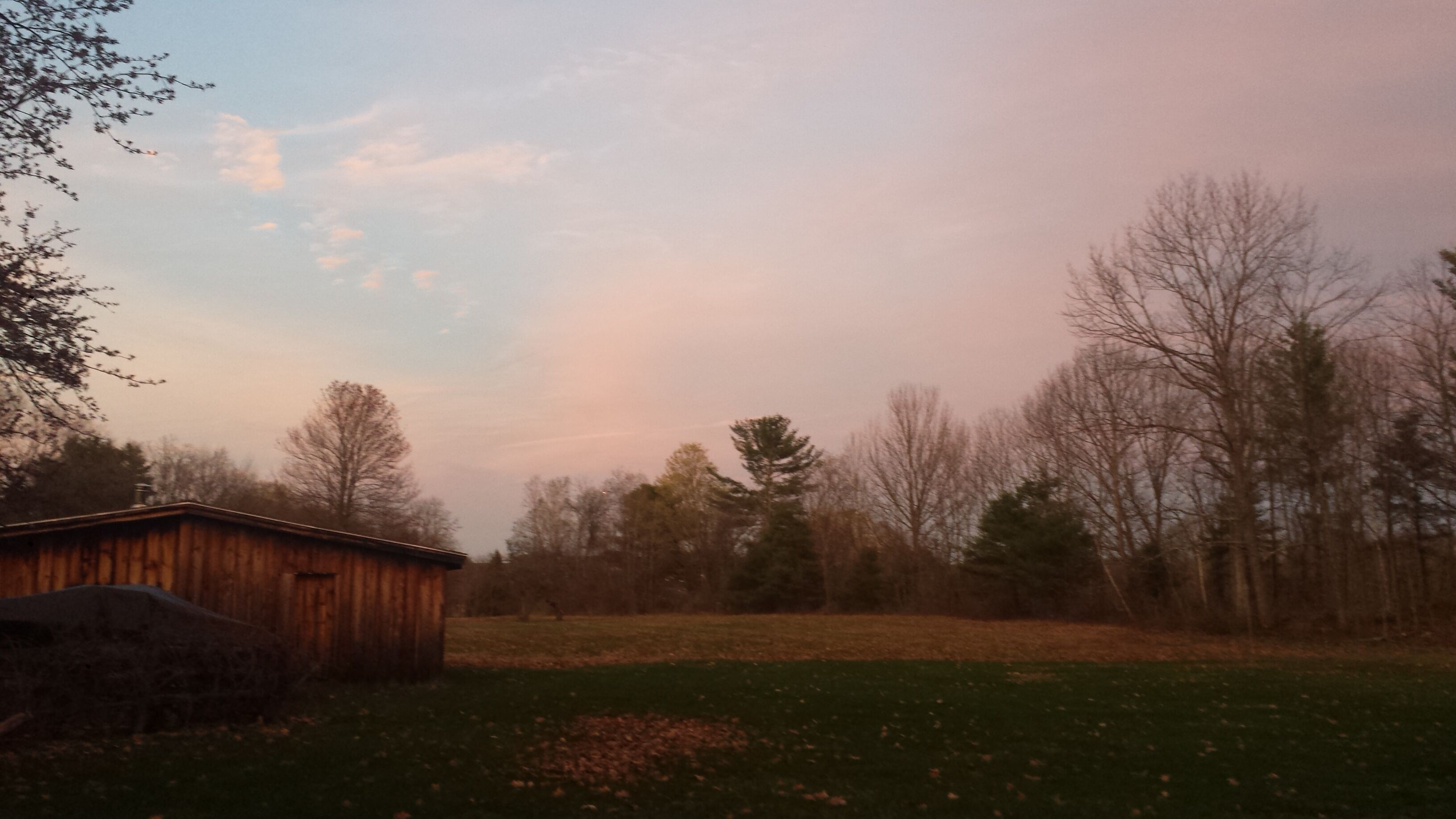 A rural landscape with a wooden barn, open fields, and leafless trees.