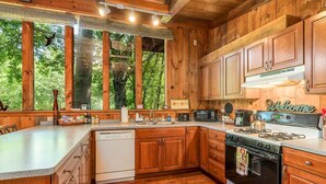 A wooden cabin-style kitchen with a large island, built-in appliances, and a view of the forest.