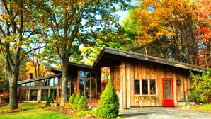 A rustic cabin with a red door, surrounded by trees with autumn foliage.