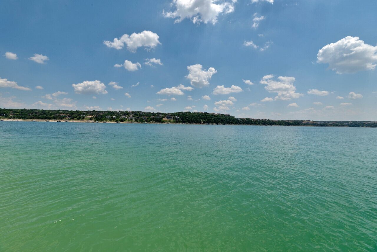 Une vue sur la côte, avec une eau turquoise et limpide, une plage de sable et une ligne côtière lointaine parsemée de bâtiments et de verdure.