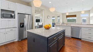 A modern kitchen with white cabinetry, stainless steel appliances, and a central island with a fruit bowl.