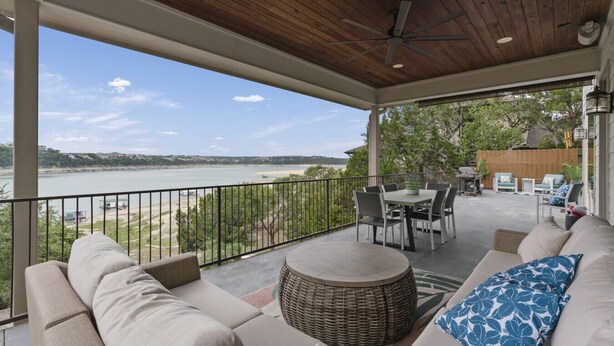 A covered patio with a view of a lake, outdoor furniture, and a dining area.