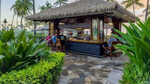An outdoor bar with a thatched roof, surrounded by lush greenery and palm trees.
