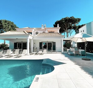 A modern building with a swimming pool, outdoor seating, and a clear sky.