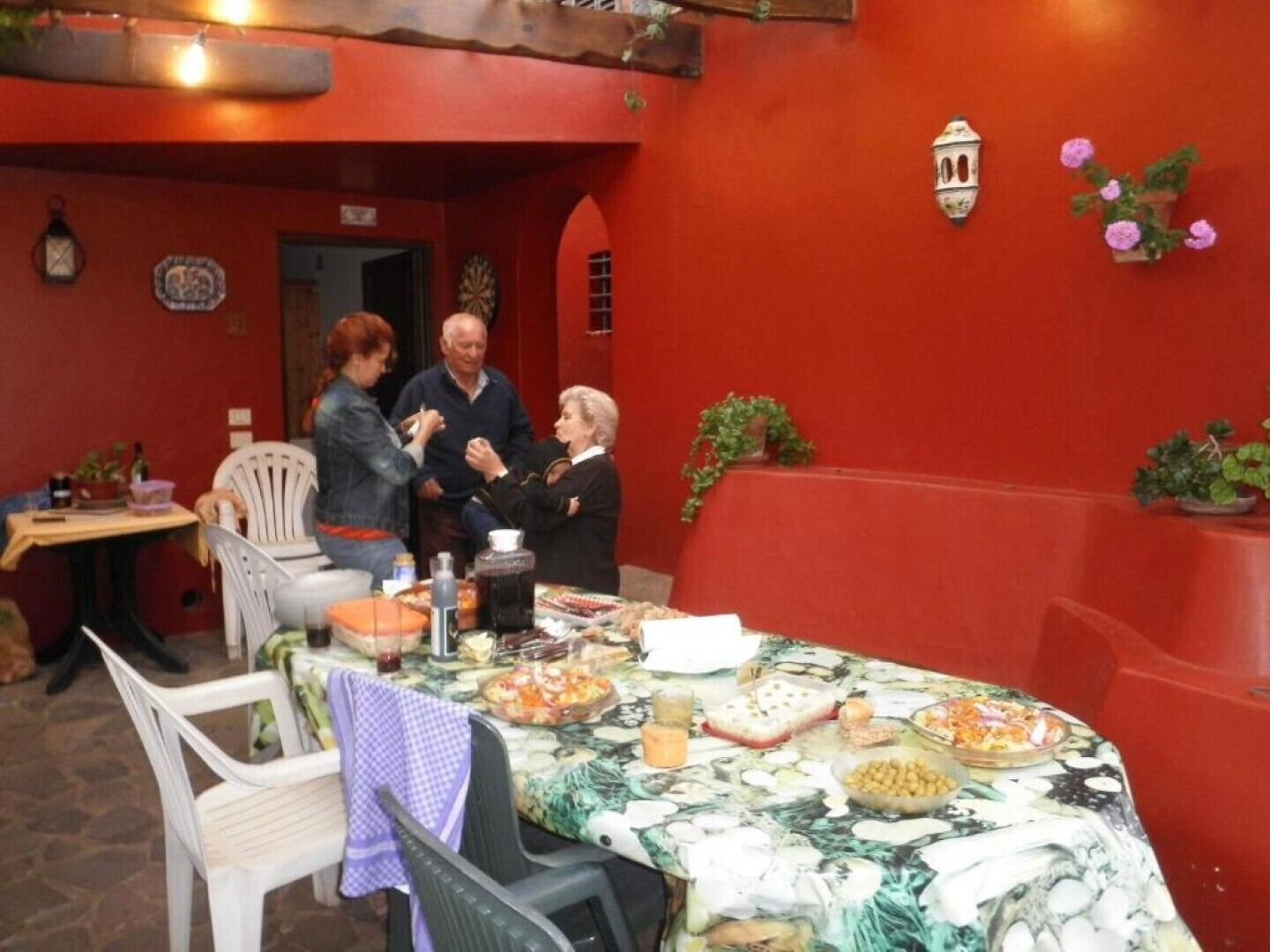 A dining area with a table set for a meal, surrounded by chairs, and a red wall with decorative elements.