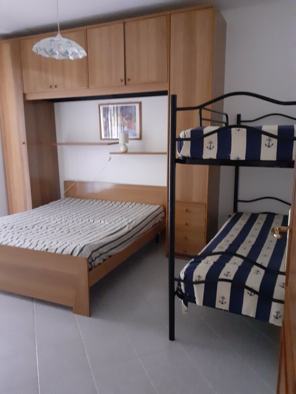 A bedroom with a bunk bed, a wooden wardrobe, a bedside table, and a hanging light fixture.