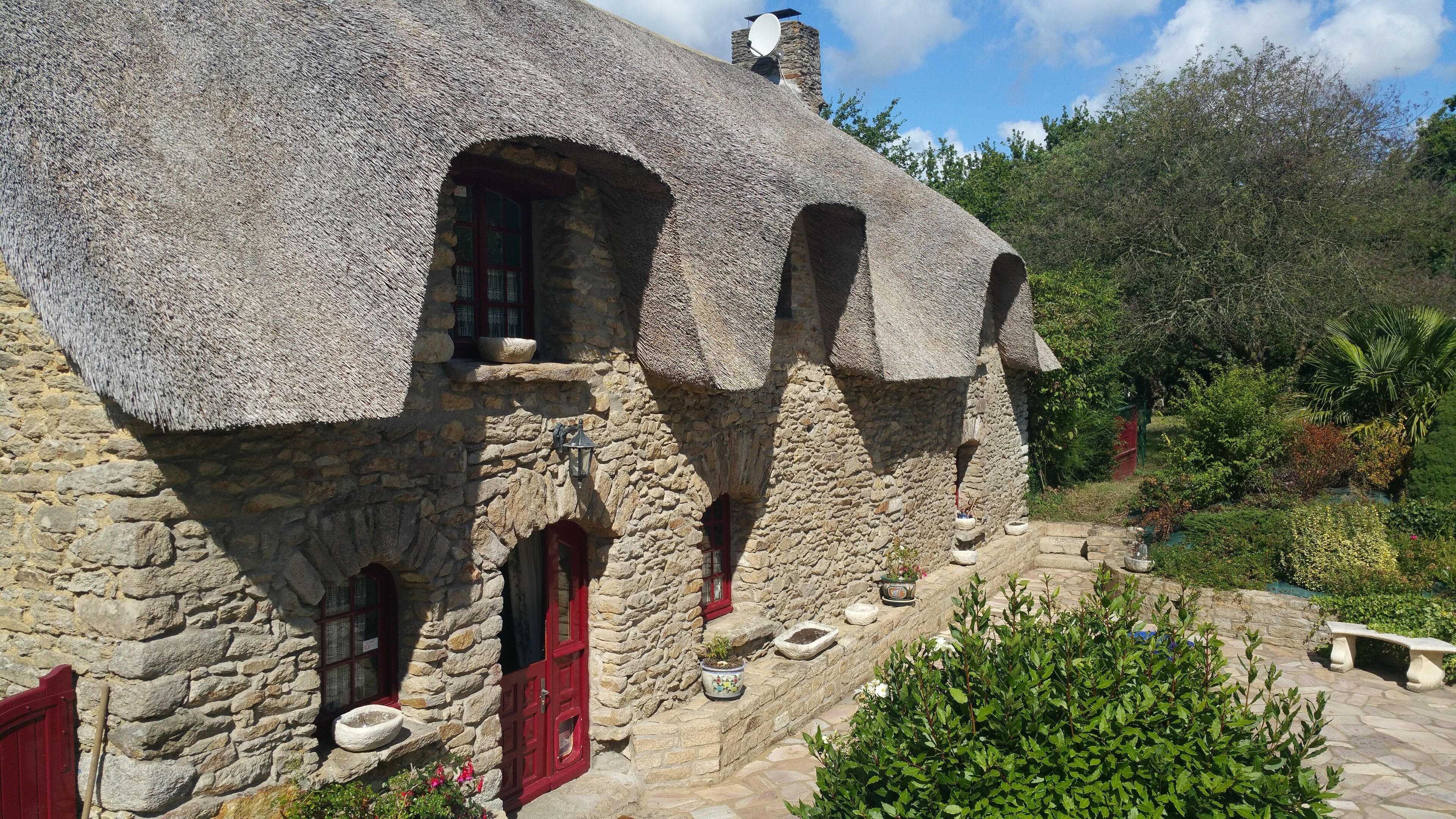 Ein Steinhaus mit Strohdach, zahlreichen Fenstern und einer roten Tür.