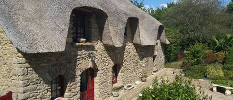 Ein Steinhaus mit Strohdach, zahlreichen Fenstern und einer roten Tür.