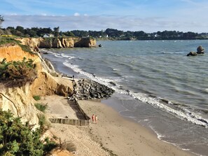 Ein Küstenstrand mit einer felsigen Klippe, einer Holzpromenade und einem Sandufer.