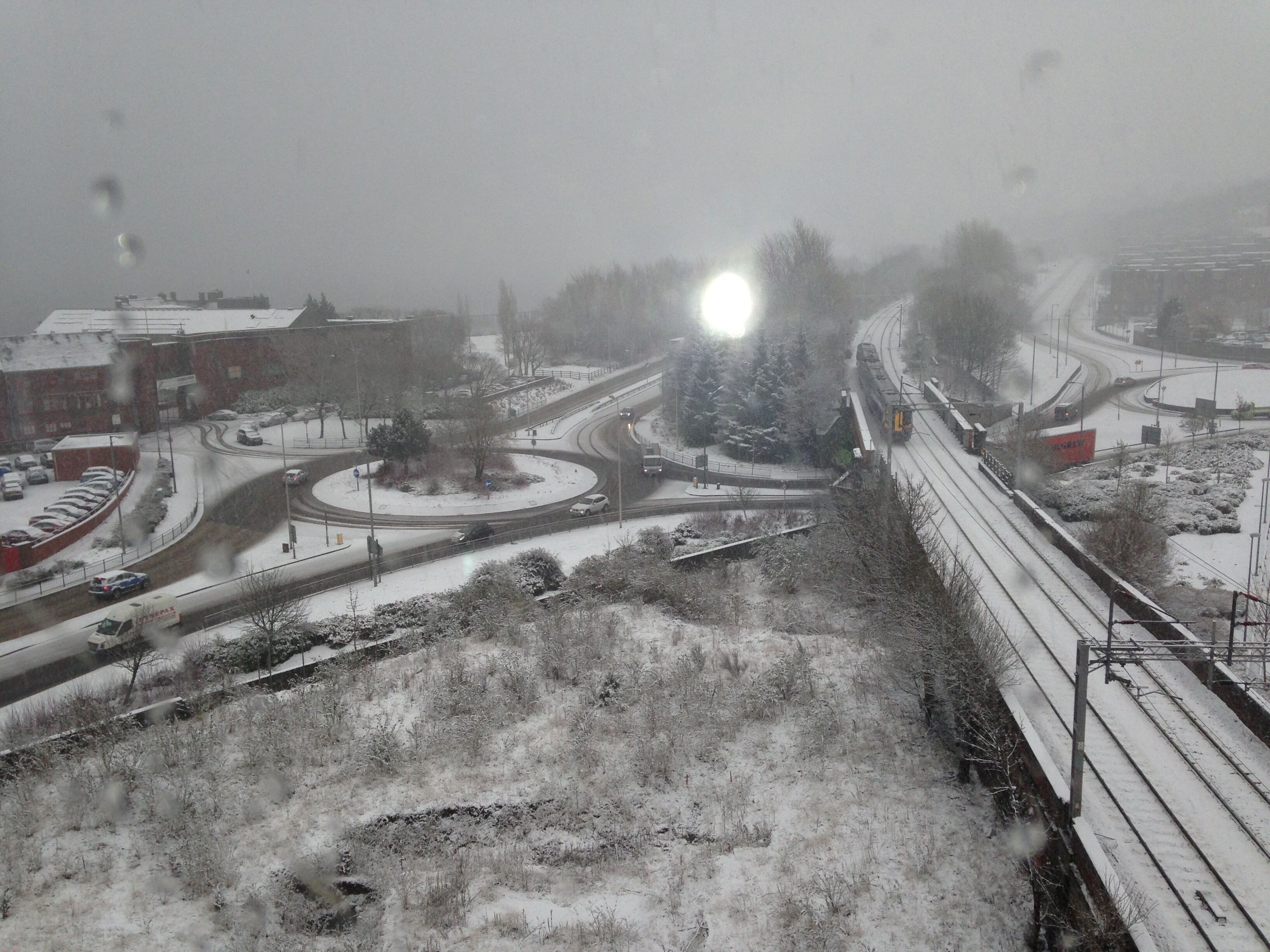 Ett snötäckt stadsmiljö med en rondell, ett järnvägsspår och en byggnad med ett rött tak.