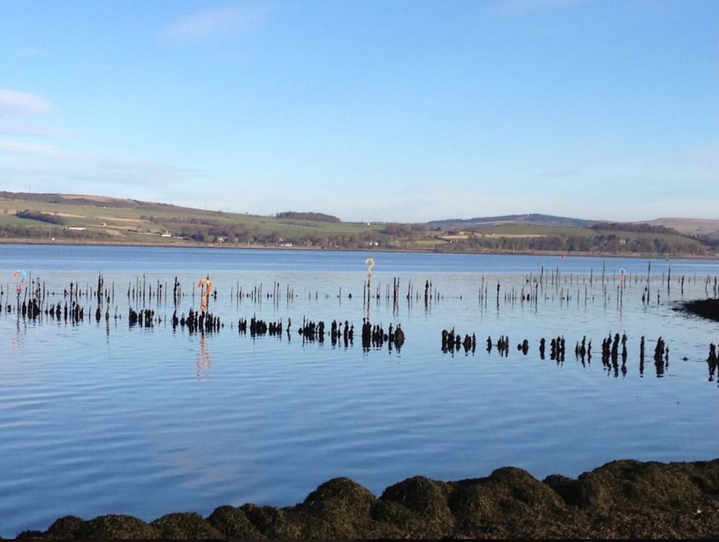 A calm lake with a rocky shoreline and distant hills.