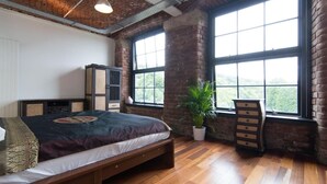 Un dormitorio con una cama grande, una planta en maceta, un aparador y una ventana con vistas a la vegetación.