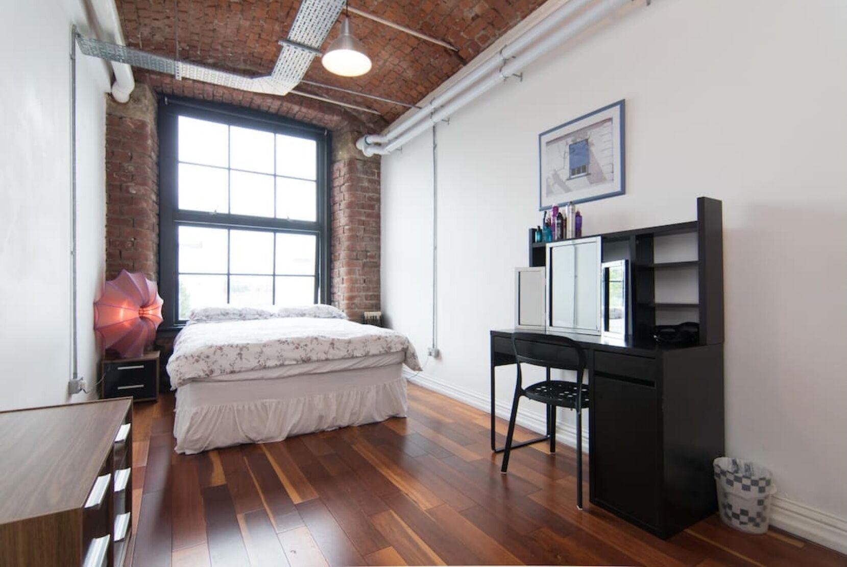 Een slaapkamer met een bed, een bureau en een groot raam.