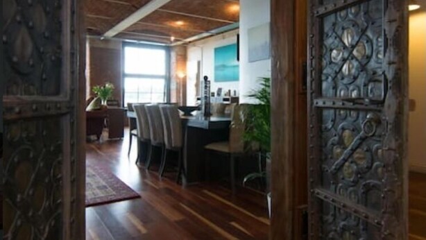 Un interior rústico con techo de madera, una zona de comedor con sillas y una mesa, y una gran puerta metálica decorativa.