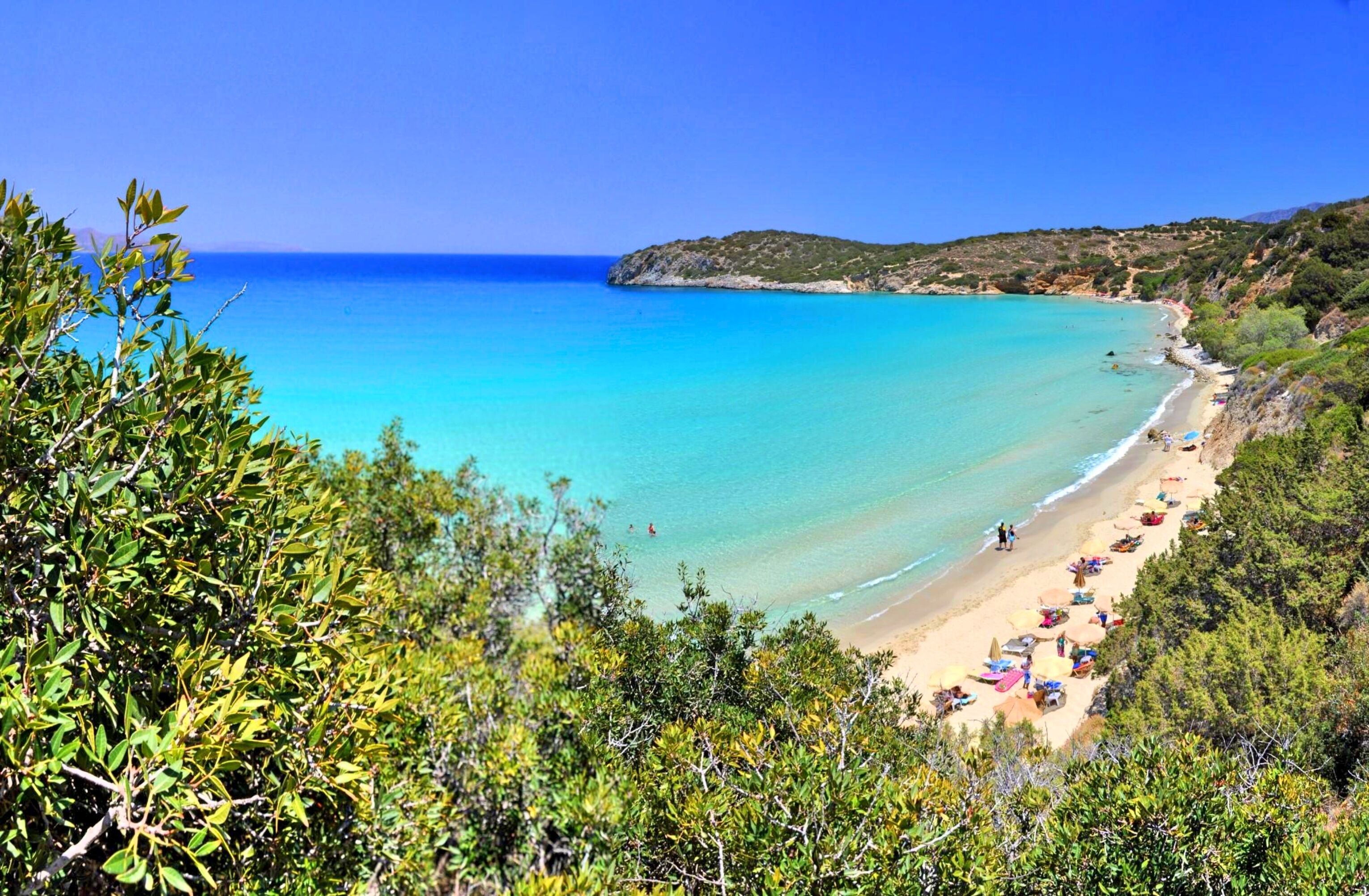 A coastal beach with clear turquoise waters, a sandy shore, and lush greenery.